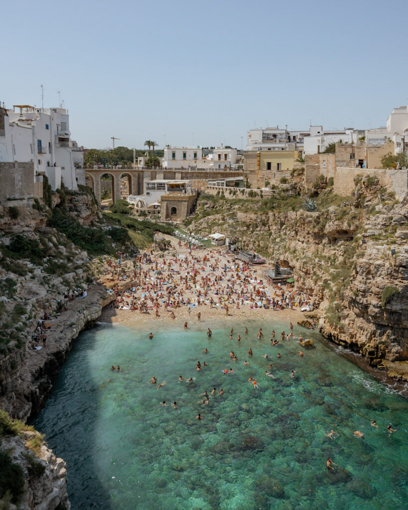 Puglia Itinerary: a high view of a beach full of people and azure-blue seawater.